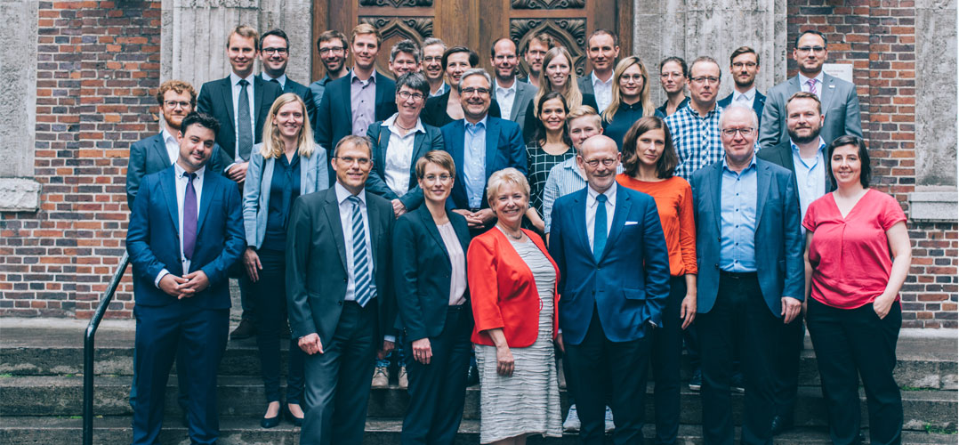 Das Bild zeigt 30 Personen, die vor einem Gebäude auf einer Treppe stehen und als Gruppe einen anschauen.