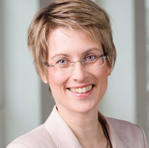 Das Bild zeigt ein Portrait von Dr. Sandra Garbade, der Geschäftsführerin des HIBB. Sie hat eine blonde Kurzhaarfrisur, einen hellen Hautton und lächelt freundlich. Sie trägt einen rosa Blazer, eine rahmenlose Brille und dezente Perlenohrringe.