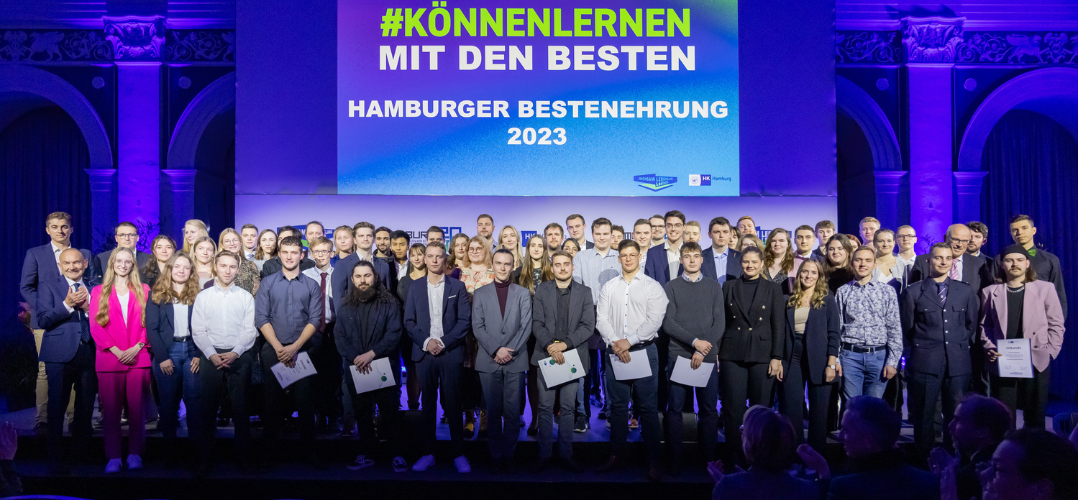 Das Bild zeigt eine Gruppe von Menschen vor einer Leinwand mit der Aufschrift "#KÖNNENLERNEN MIT DEN BESTEN - HAMBURGER BESTENEHRUNG 2023" Die Personen in der ersten Reihe halten Urkunden in den Händen.