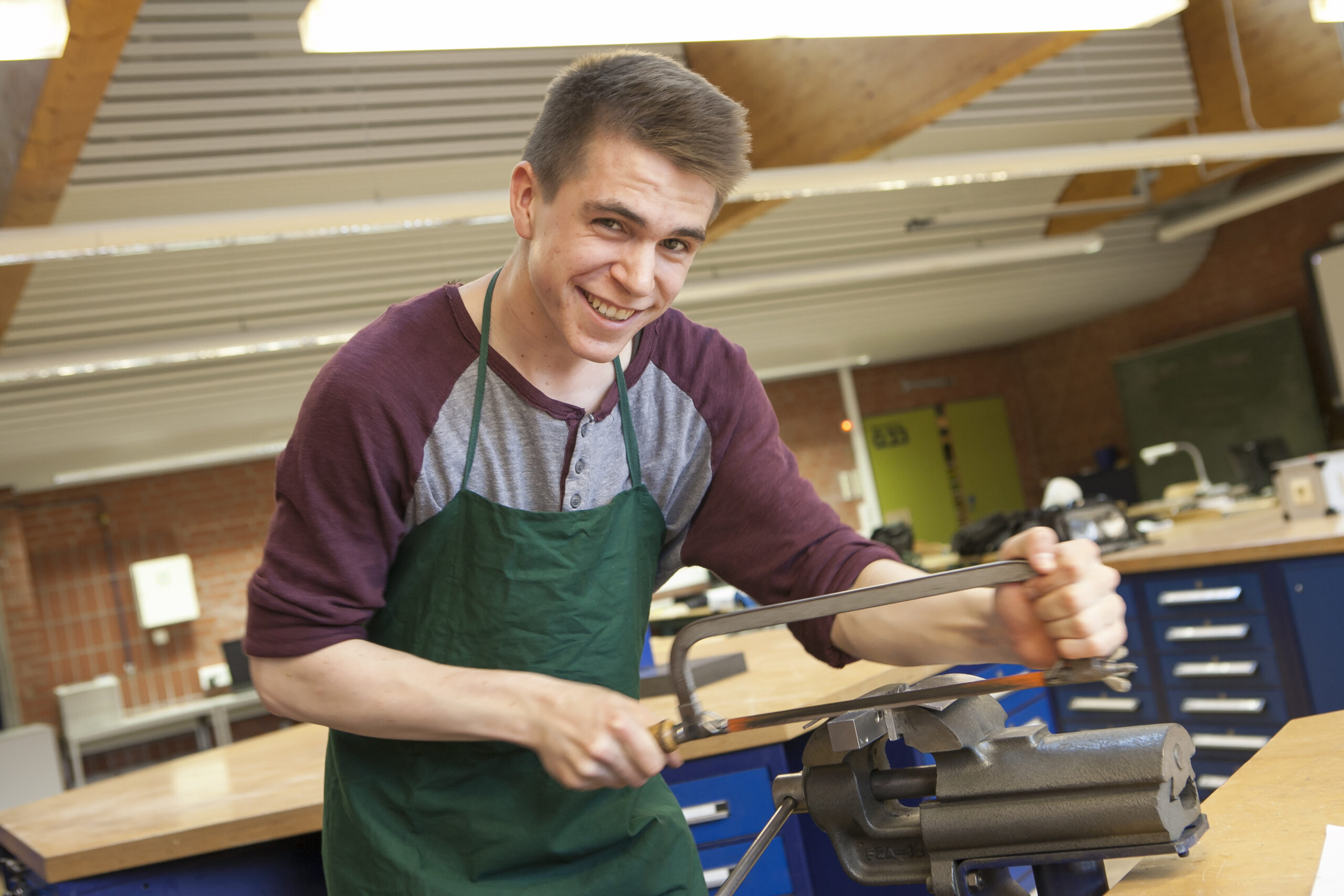 Das Foto zeigt einen jungen Mann mit Säge an einer Werkbank. Das Bild ist insgesamt dunkelblau eingefärbt.